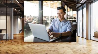 portrait of handsome asian smiling man using laptop in the cafe Wall mural